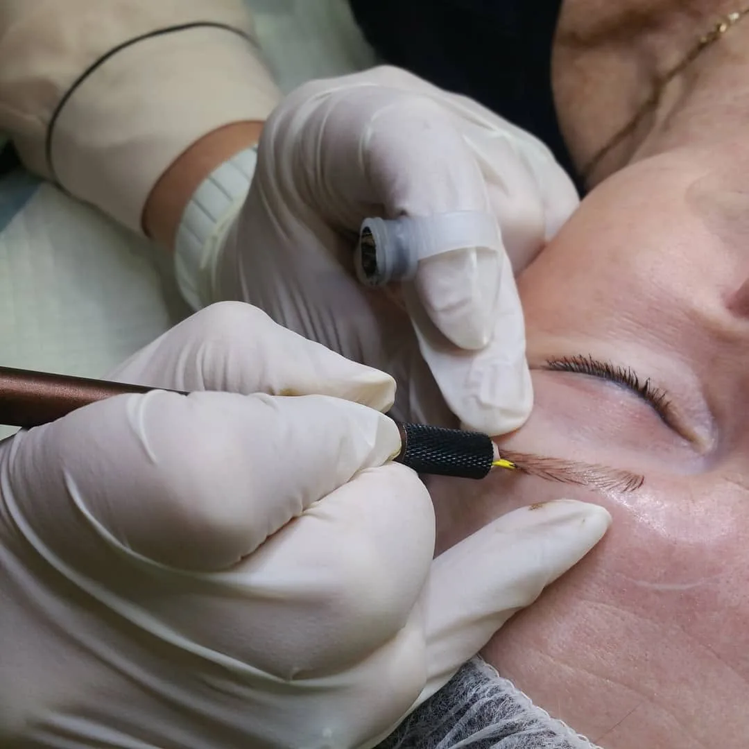 Gloved hands performing a manual brow-tattoo procedure — microblade work in progress